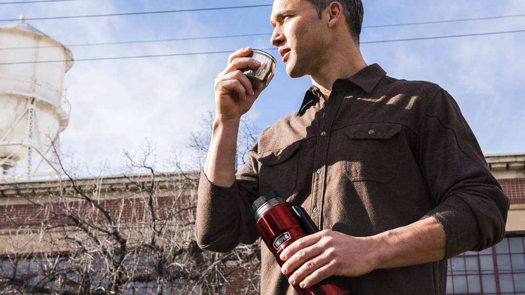 man drinking from stainless steel thermos